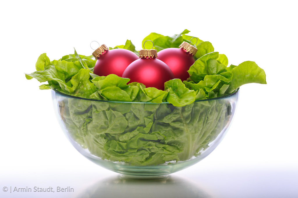a bowl with fresh salad and three red christmas balls