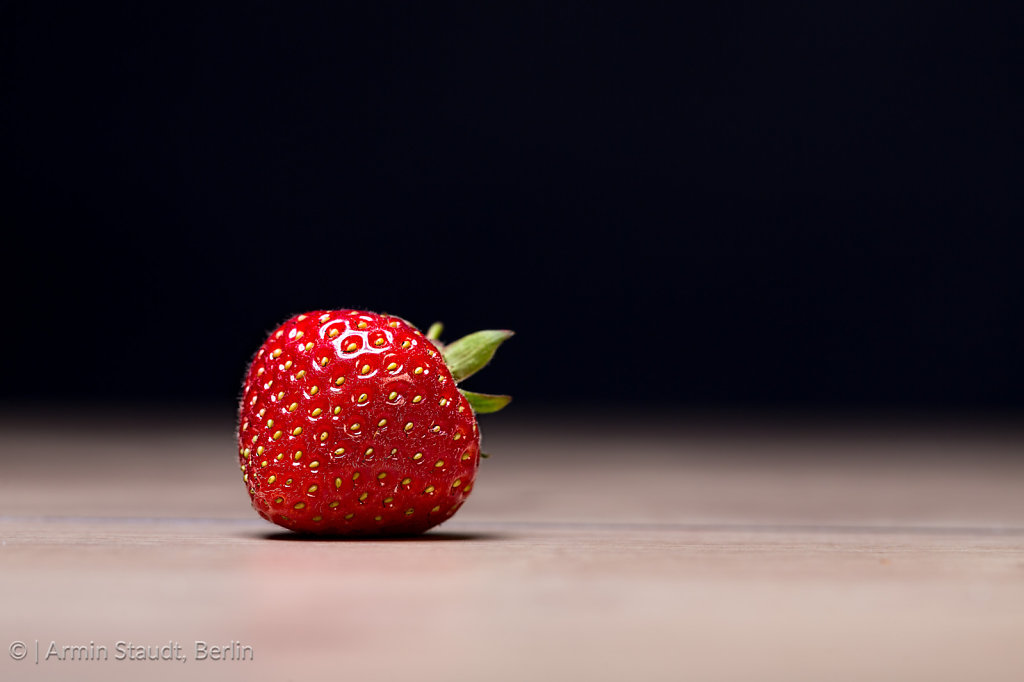single strawberry on a table with black background