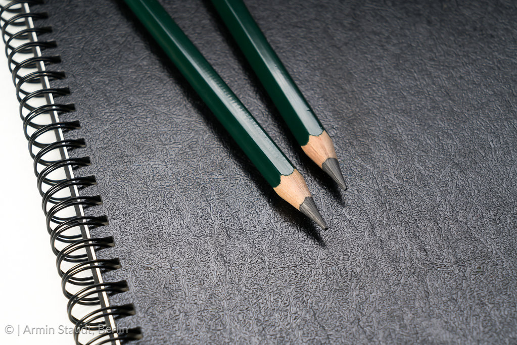 two green pencils laying on a black ring binder